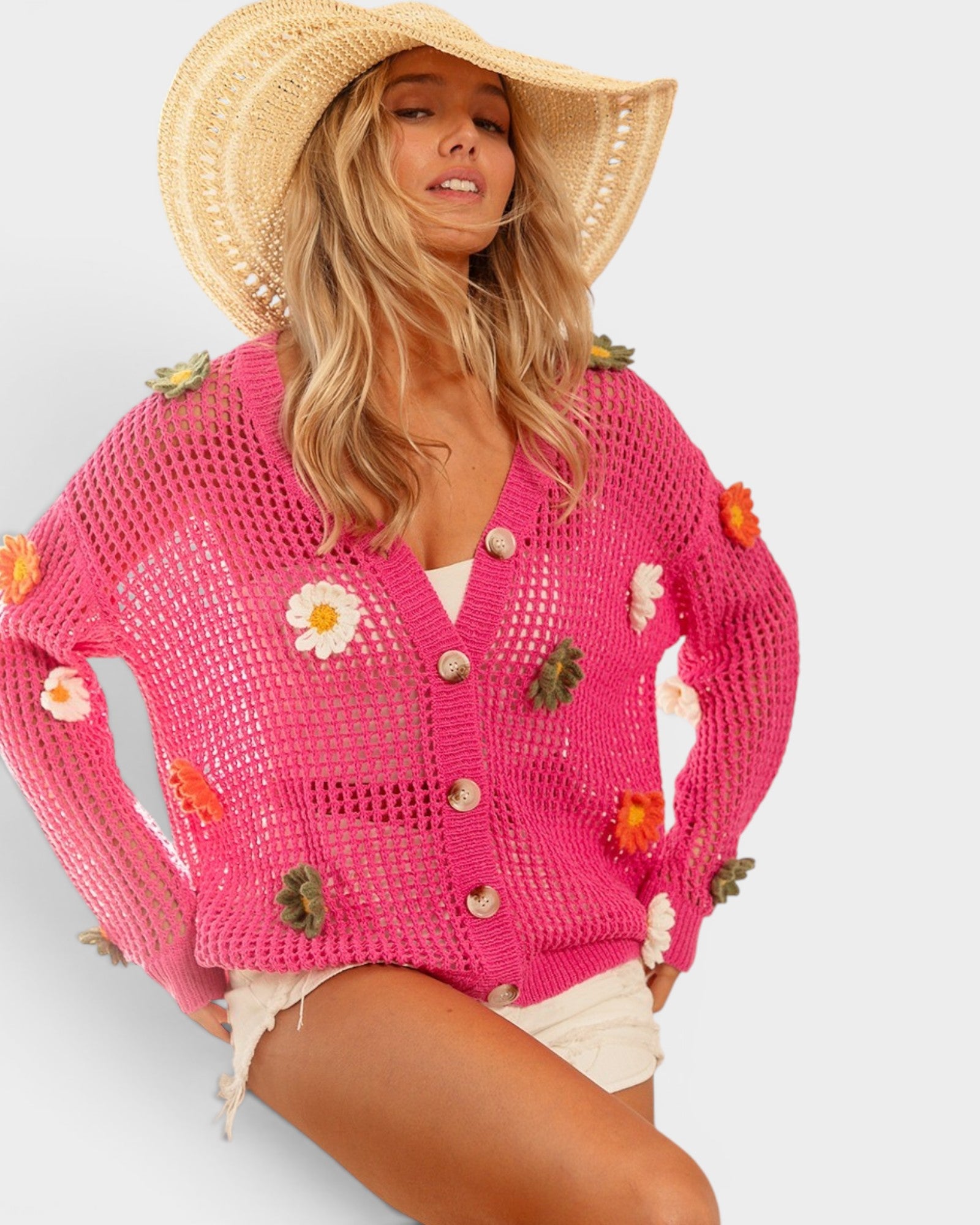 Woman wearing a pink crochet cardigan with floral decorations on a light gray background