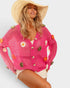 Woman wearing a pink crochet cardigan with floral decorations on a light gray background
