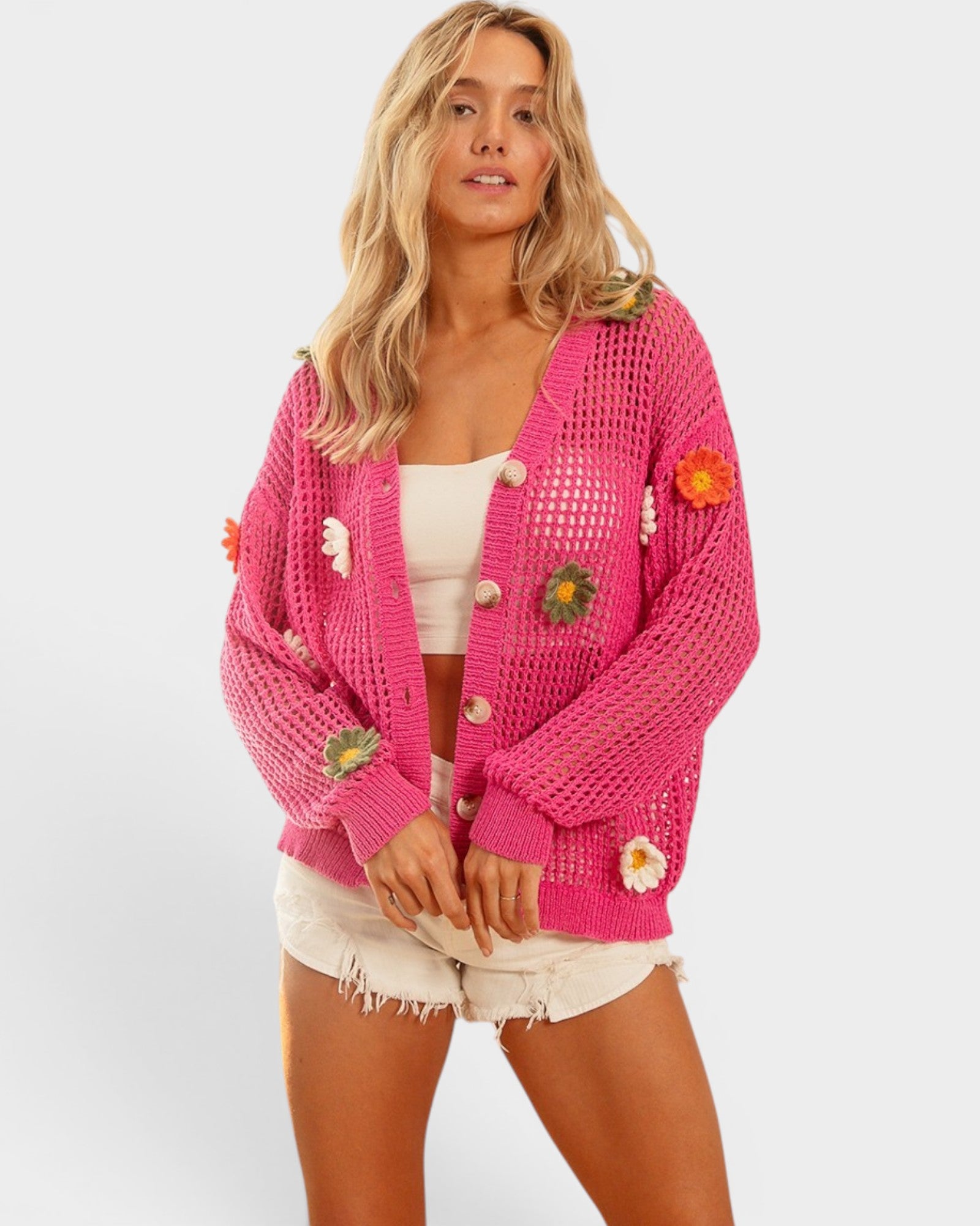 Woman wearing a pink knitted cardigan with floral embellishments on a white background