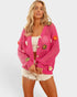 Woman wearing a pink knitted cardigan with floral embellishments on a white background