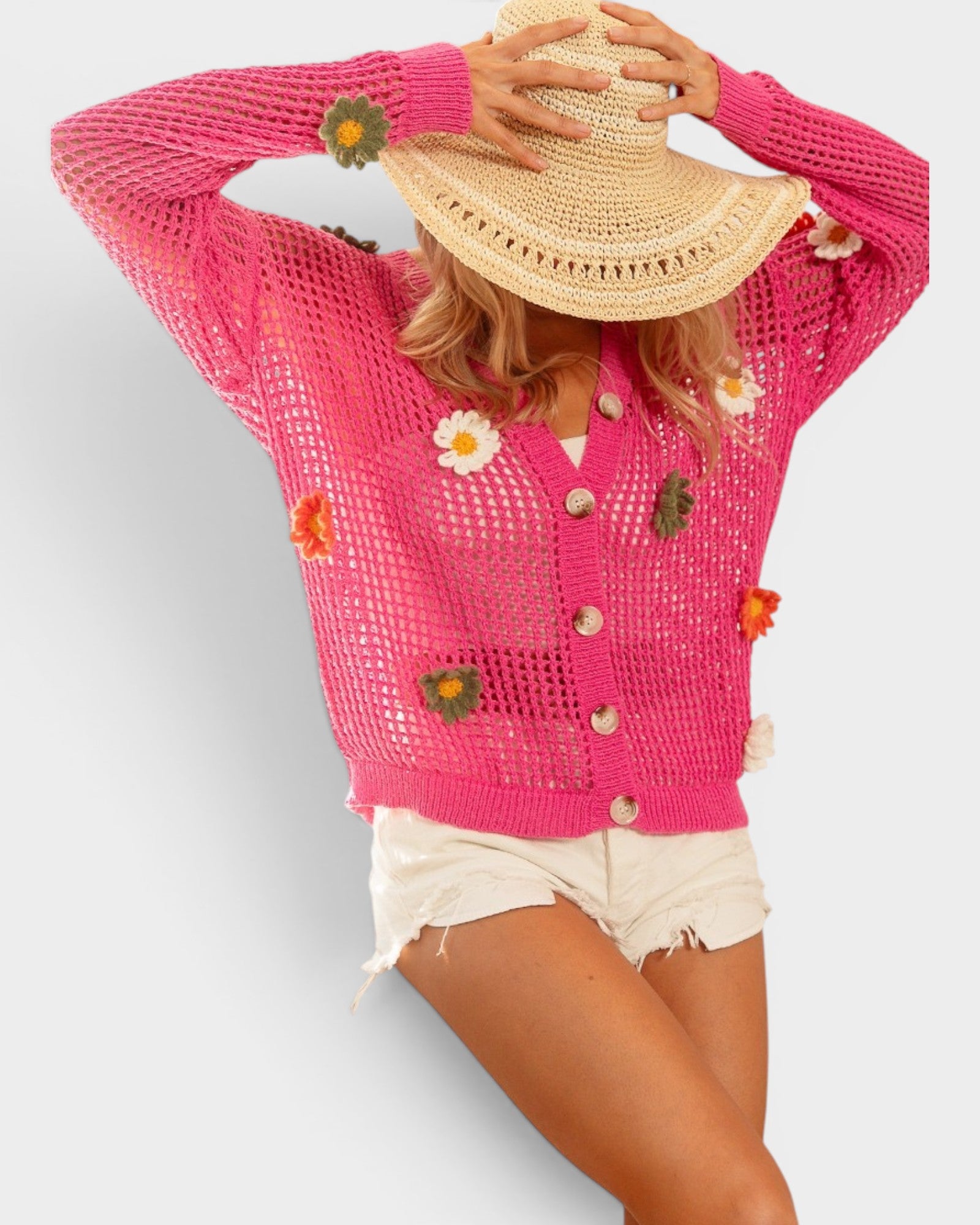 Person wearing a pink crochet cardigan with floral and button details on a plain background