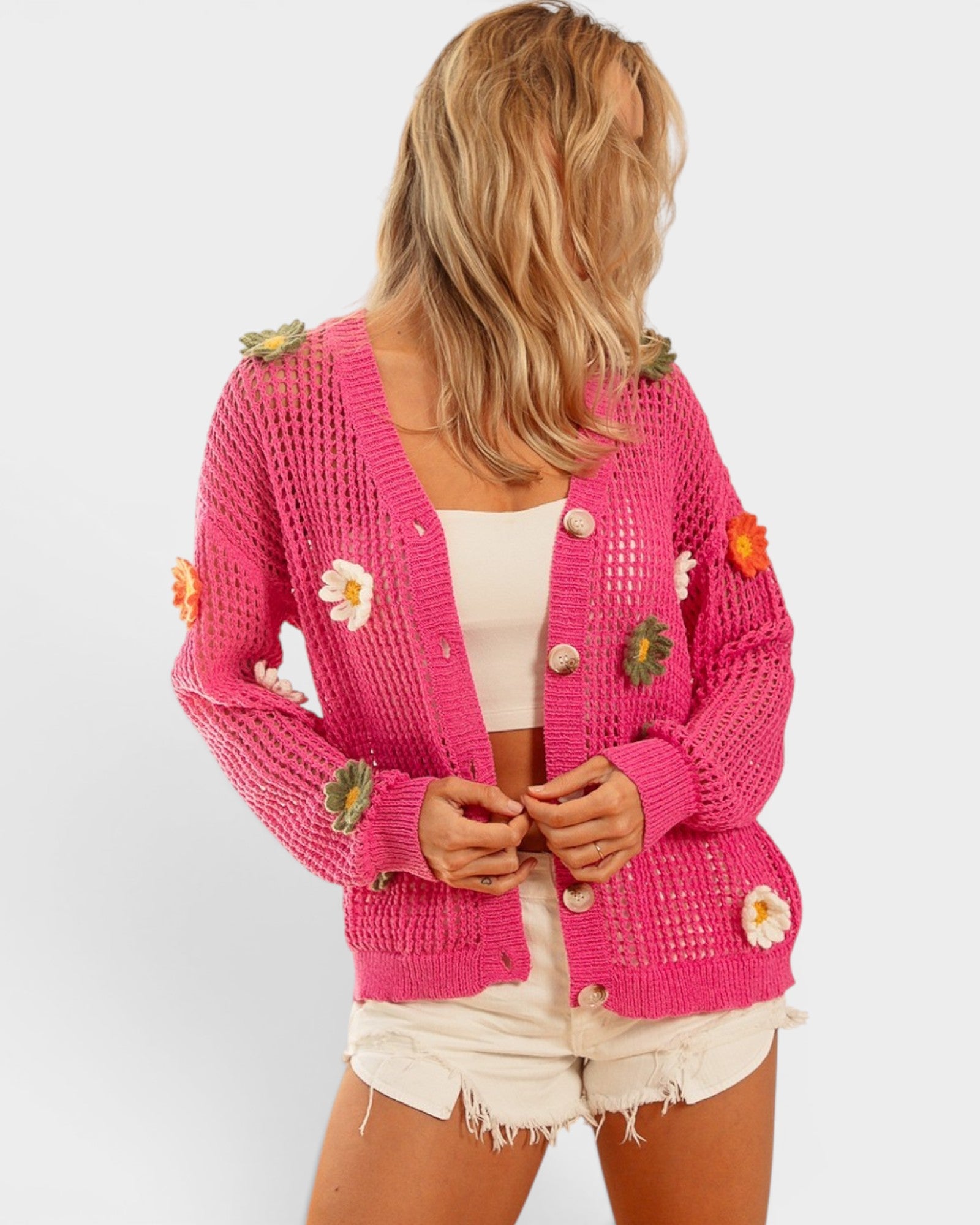 Woman wearing a pink crochet cardigan with floral embellishments on a white background