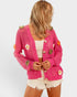 Woman wearing a pink crochet cardigan with floral embellishments on a white background