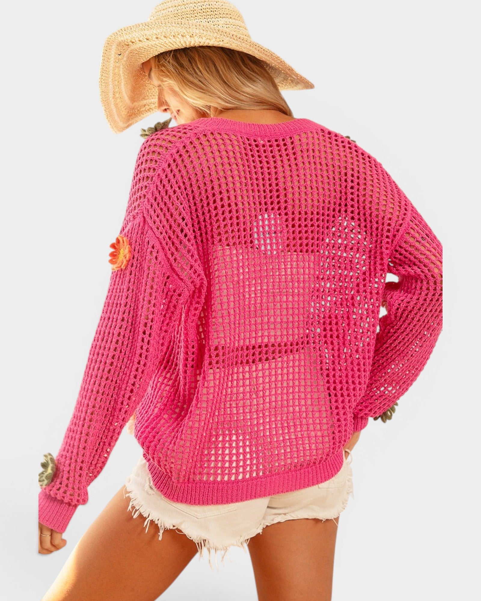 Person wearing a bright pink open-knit cardigan and straw hat on a light gray background
