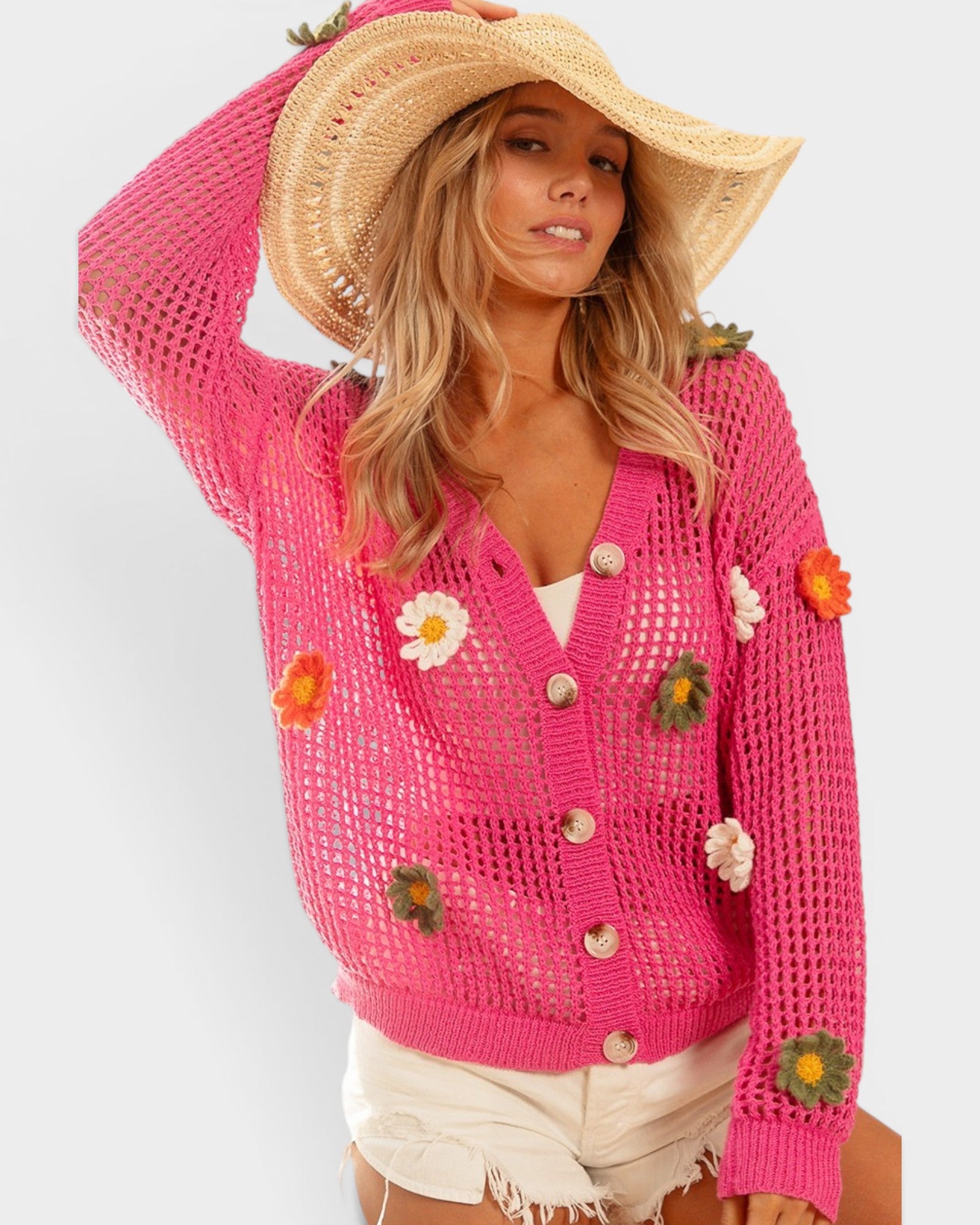 Woman wearing a pink crochet cardigan with floral embellishments on a white background