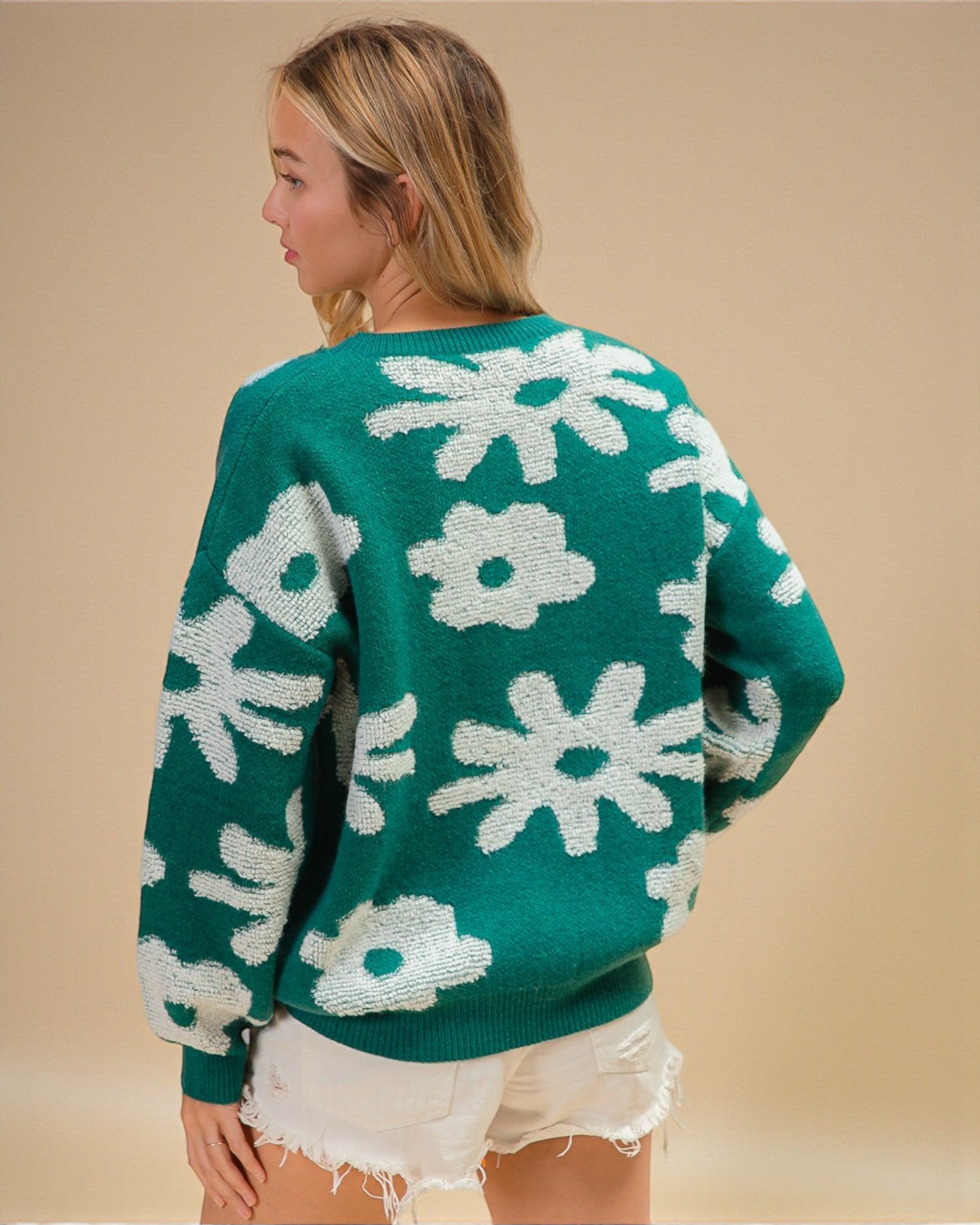 Woman wearing a green sweater with white floral patterns on a beige background