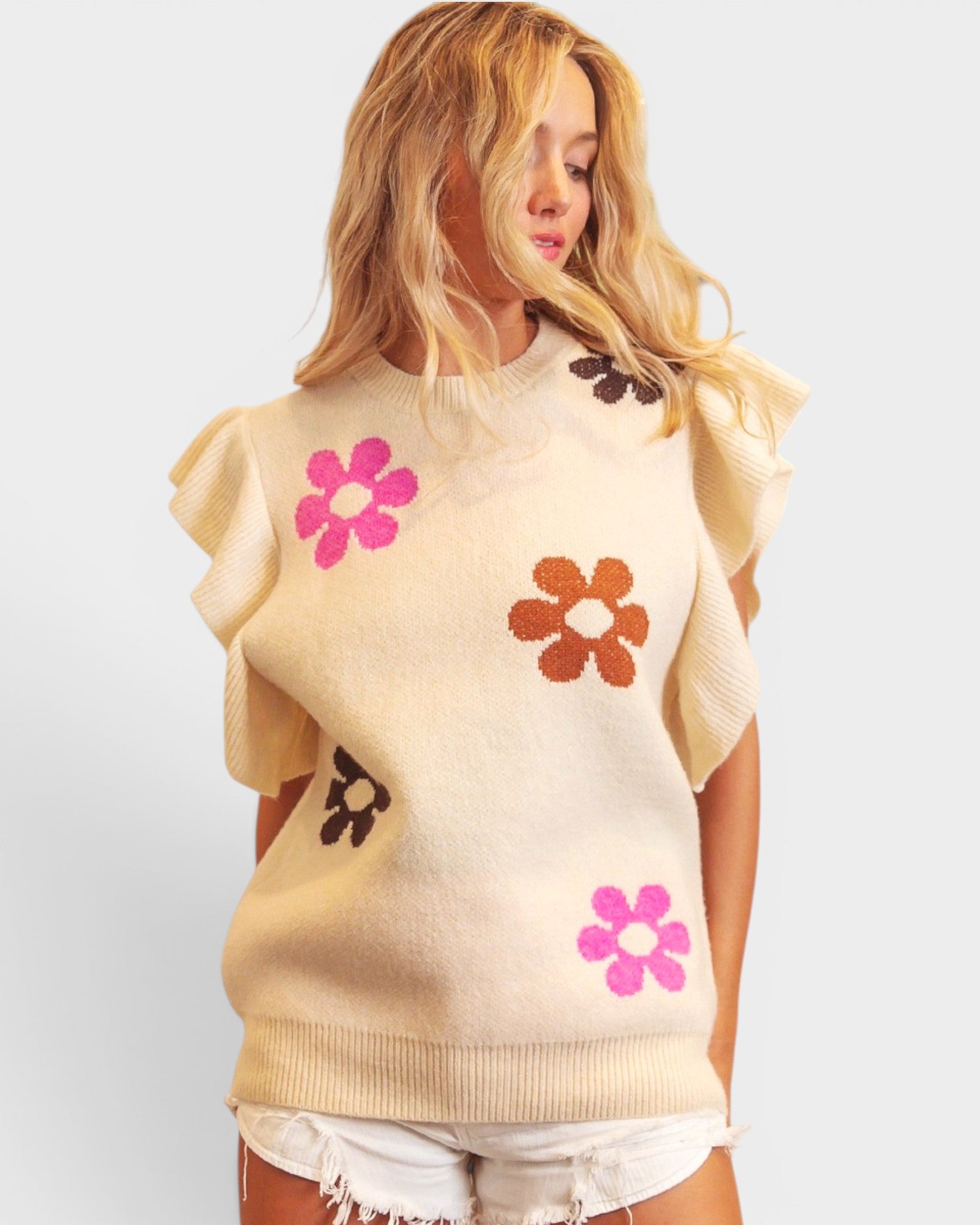 Woman wearing a sleeveless sweater with floral patterns on a plain background
