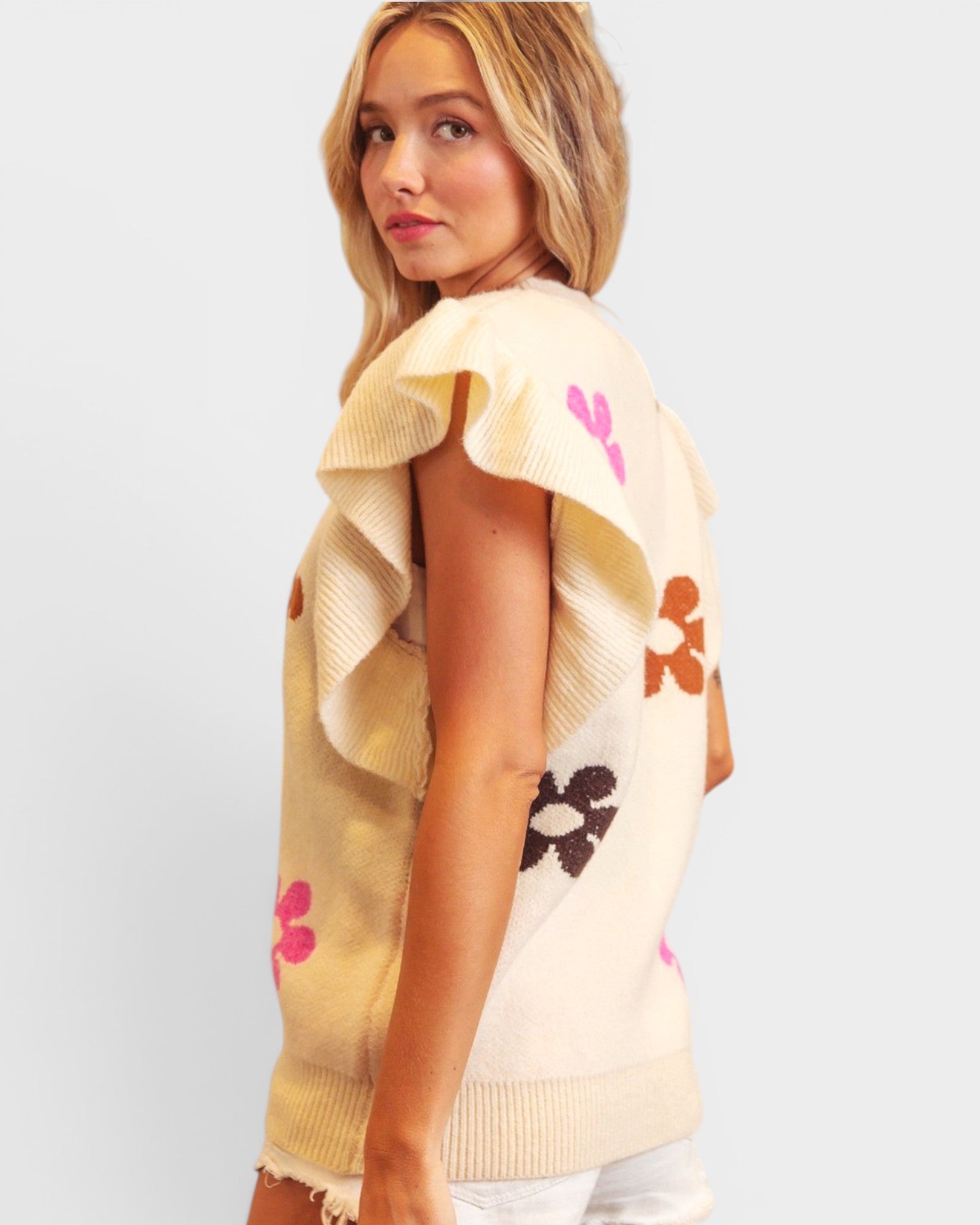 Woman wearing a beige sleeveless top with floral patterns on a plain background