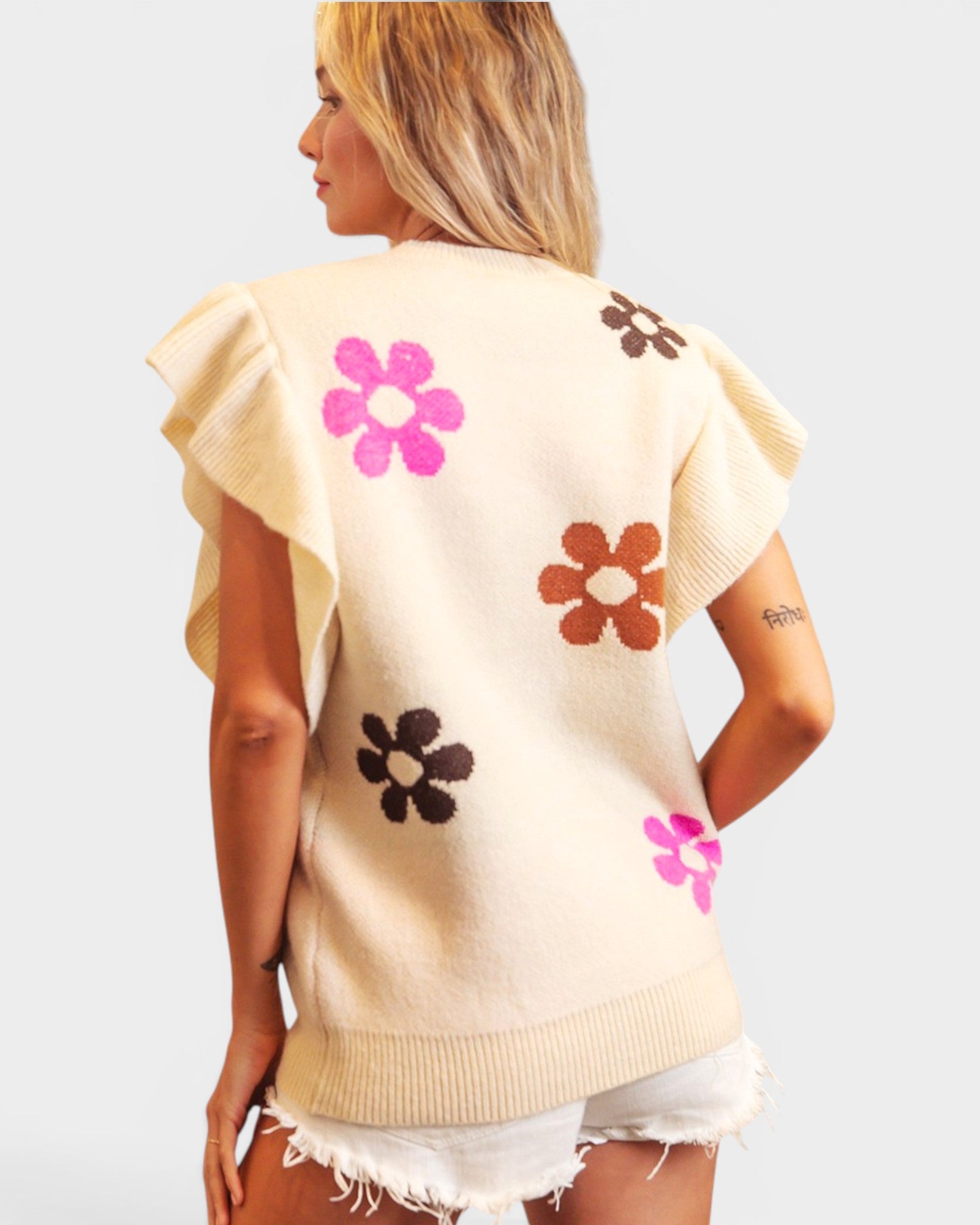 Woman wearing a beige sleeveless top with colorful flower designs on a plain background