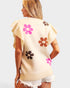 Woman wearing a beige sleeveless top with colorful flower designs on a plain background