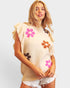 Woman wearing a sleeveless beige top with floral designs on a plain background