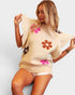 Woman wearing a beige sweater with floral designs on a plain background