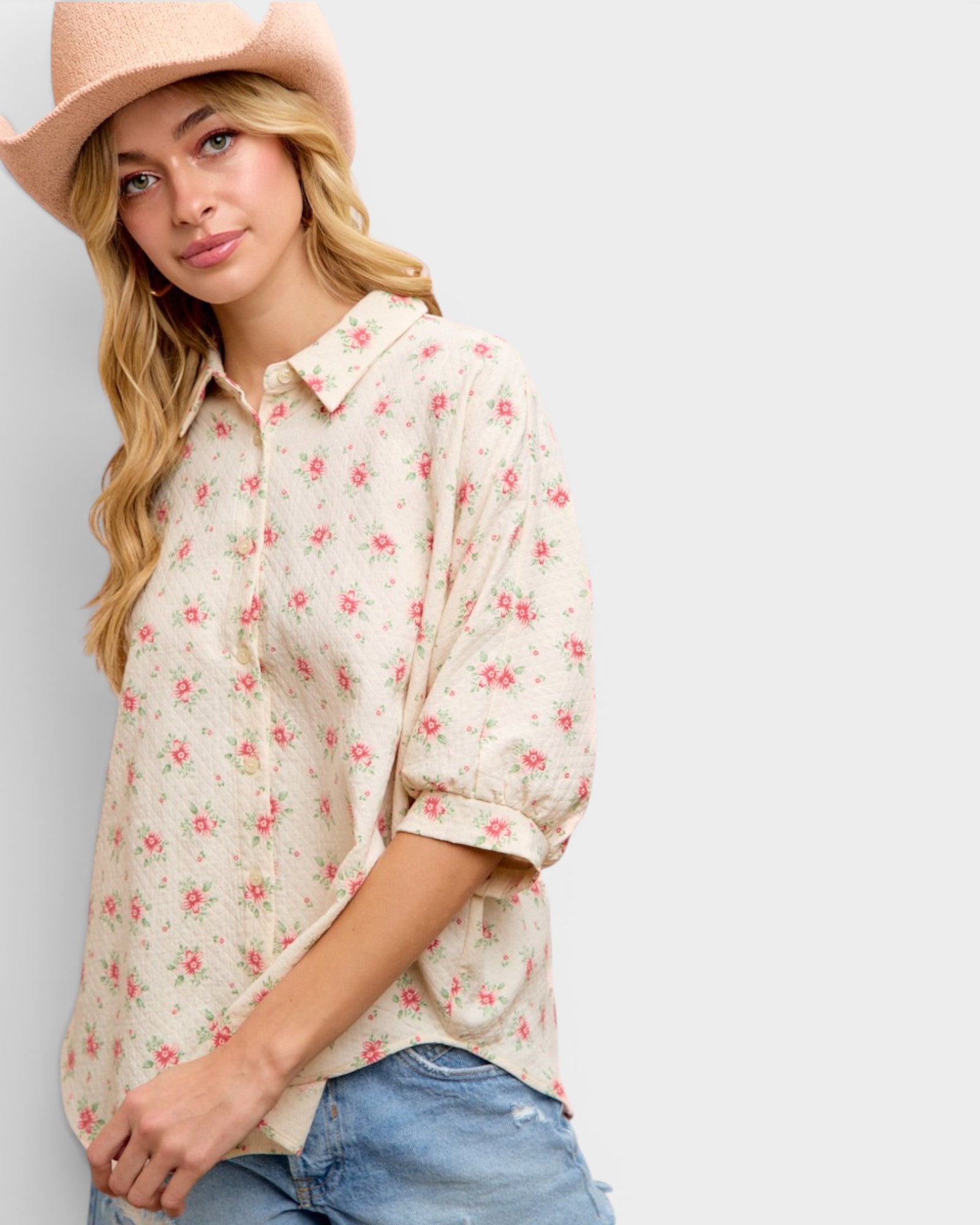 Woman wearing a floral blouse and hat against a plain background