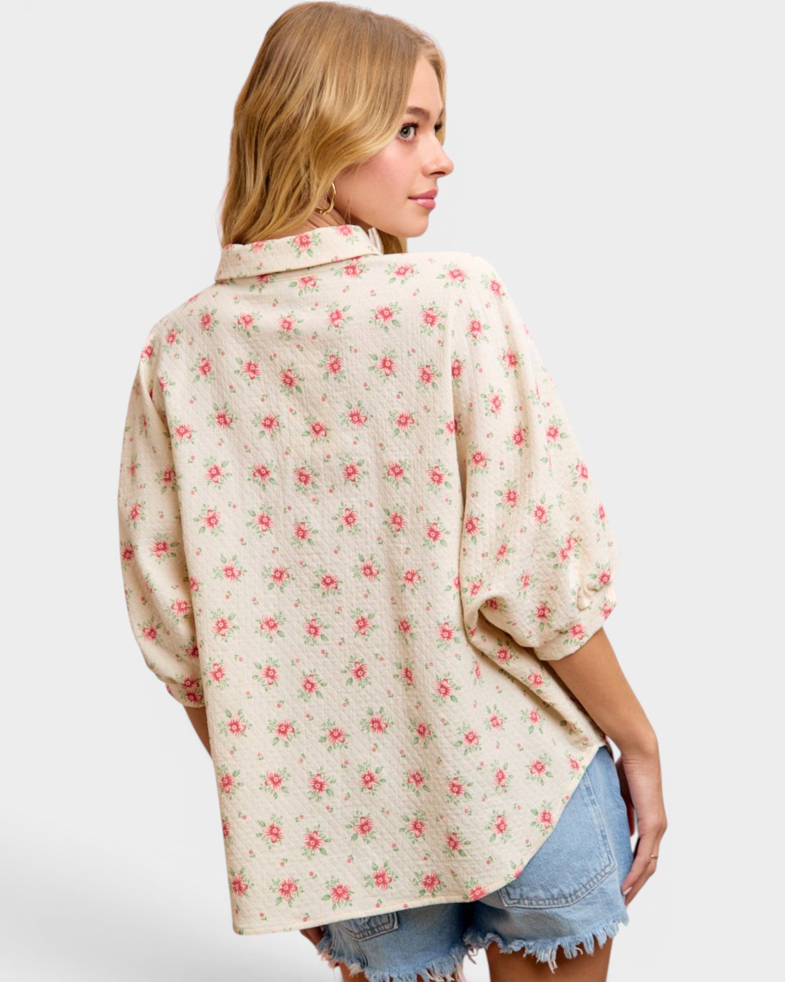 Woman wearing a floral patterned shirt with denim shorts on a plain background