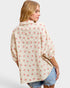 Woman wearing a floral patterned shirt with denim shorts on a plain background