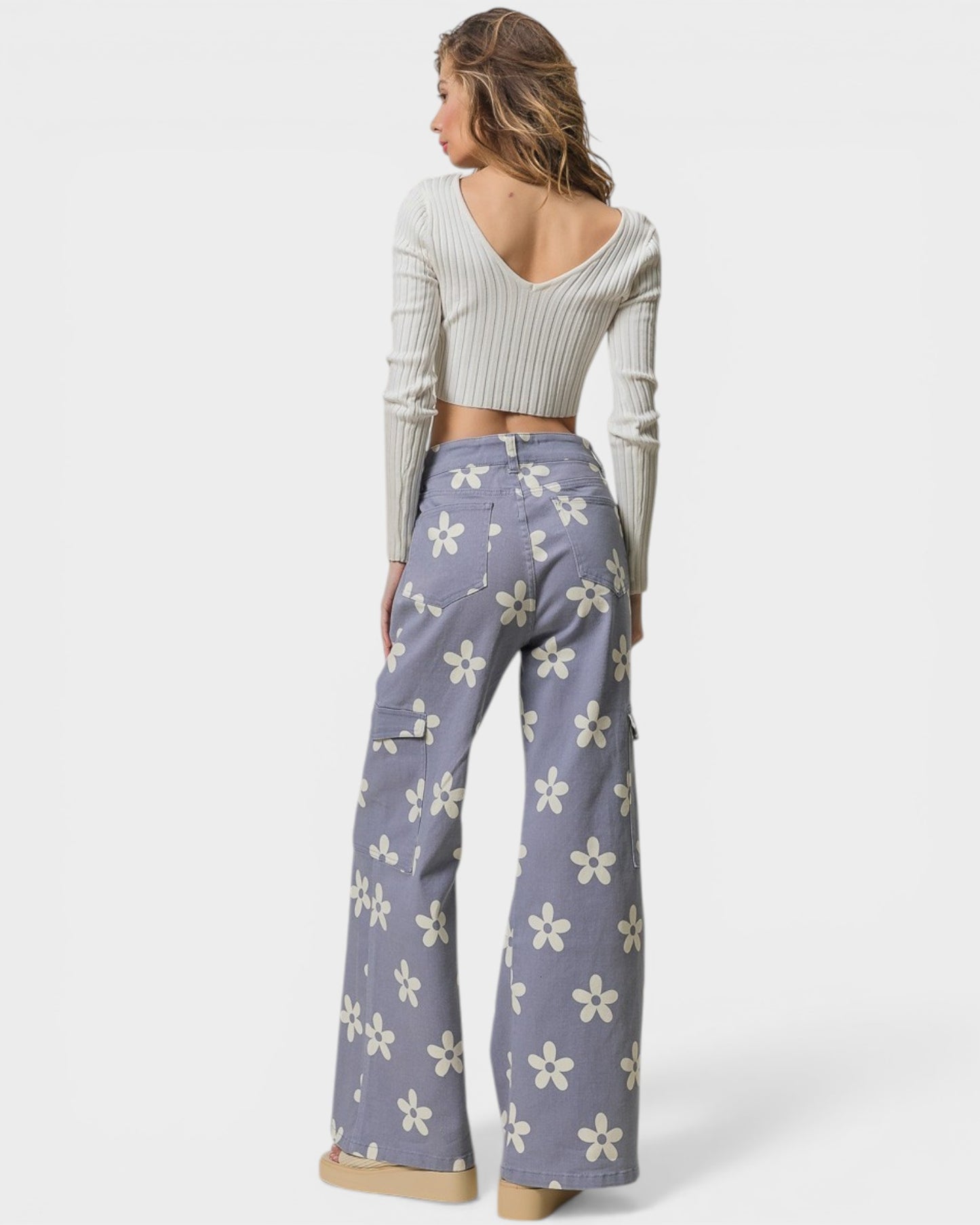 Woman wearing a light gray ribbed sweater and purple floral pants on a white background