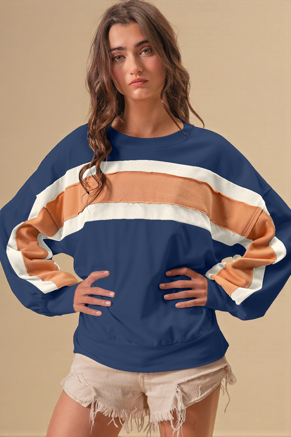 Woman wearing a blue sweater with color-blocked sleeves against a beige background