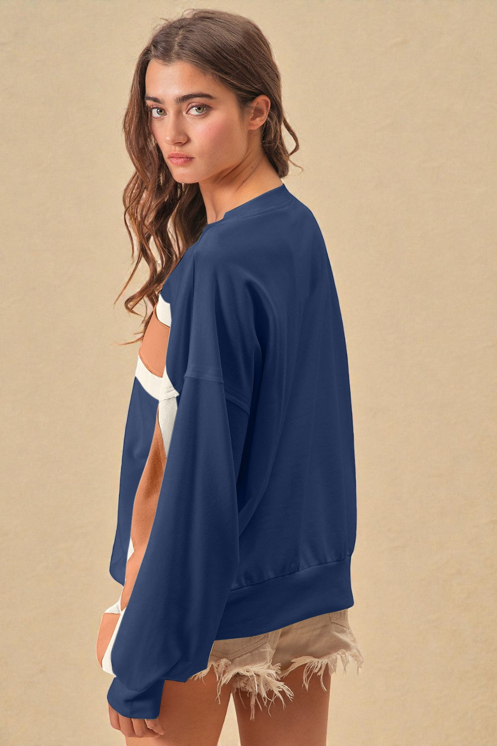 Woman wearing a navy blue sweatshirt over a white top with beige shorts on a beige background