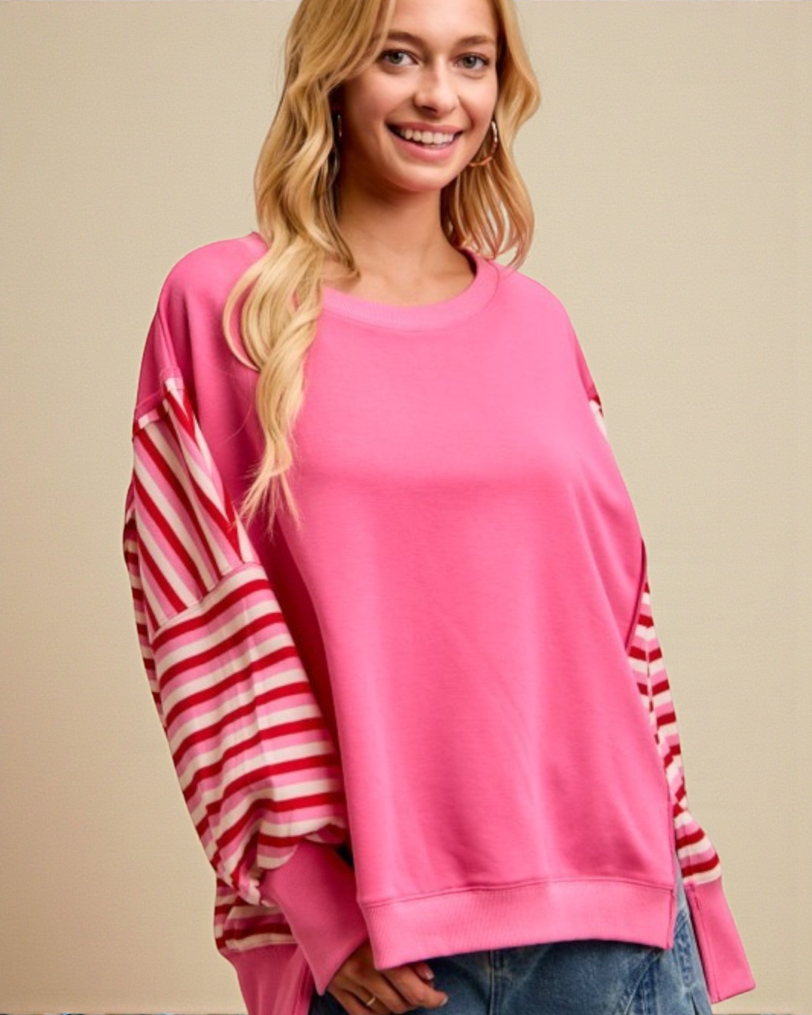 Woman wearing a pink sweater with red and white striped sleeves on a beige background