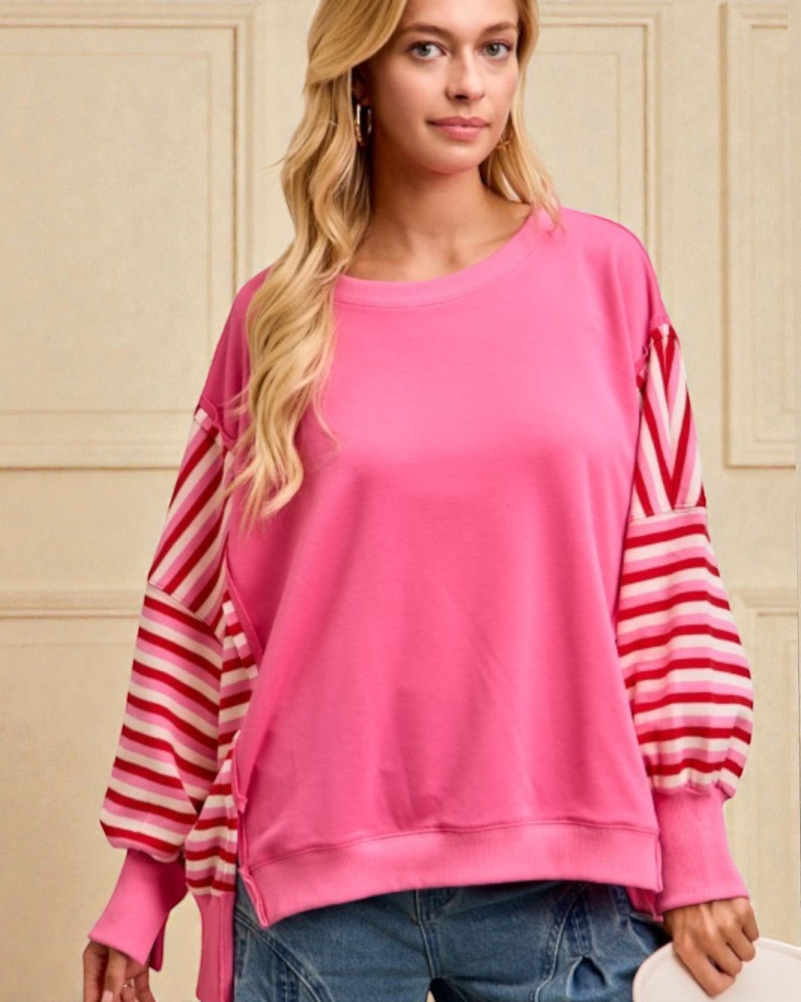 Woman wearing a pink sweater with striped sleeves against a beige wall.