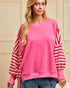 Woman wearing a pink sweater with striped sleeves against a beige wall.