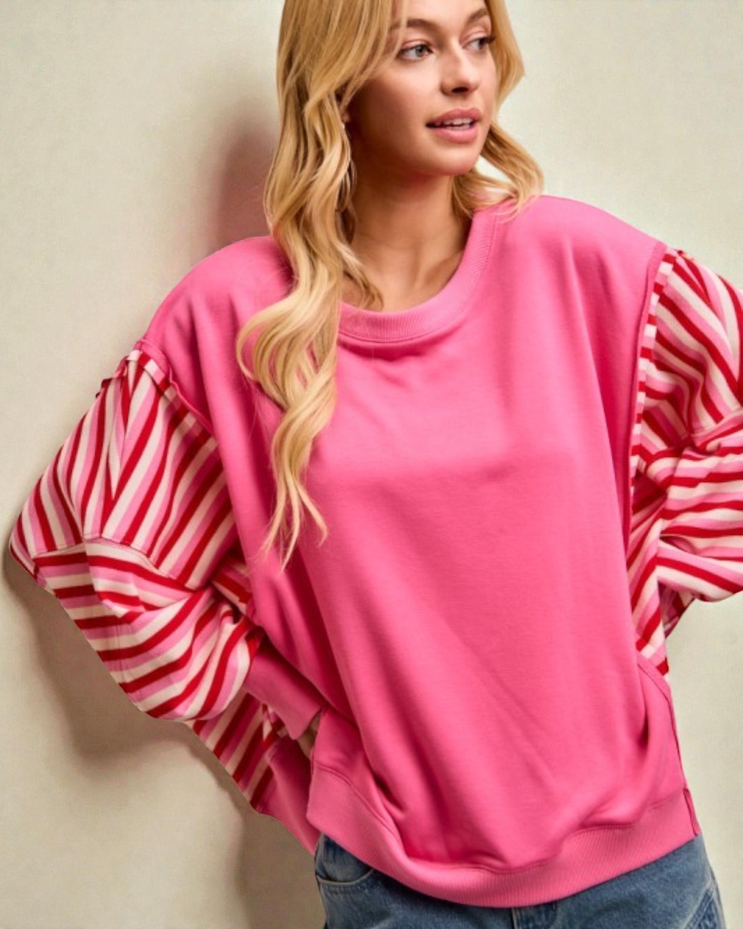 Woman wearing a pink sweatshirt with striped sleeves against a beige background