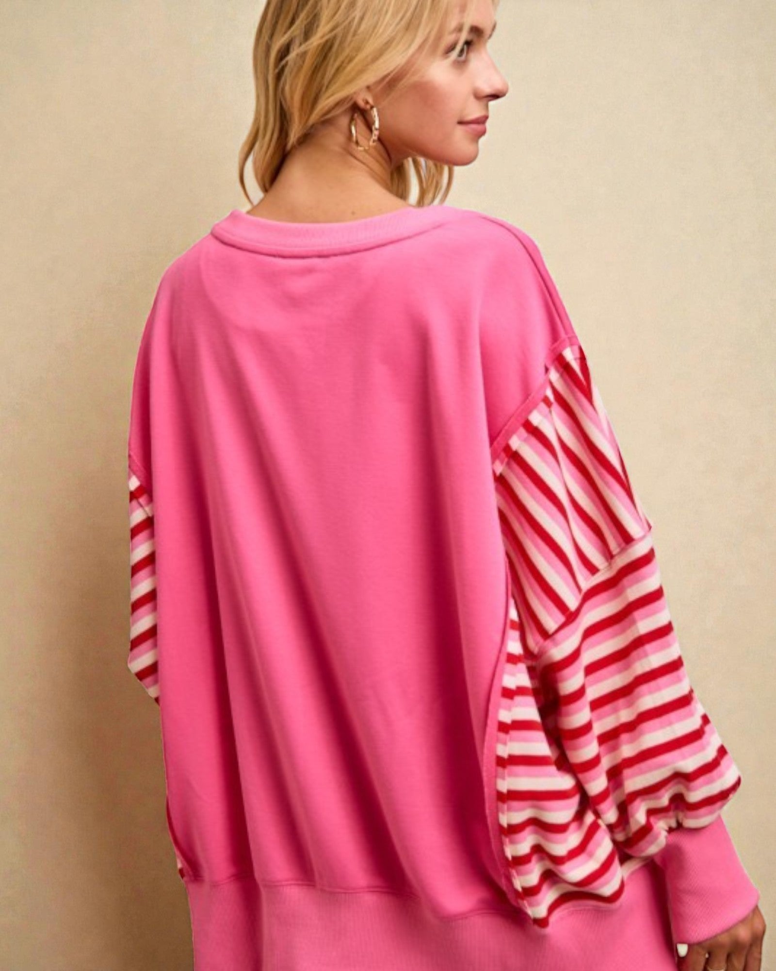 Woman wearing a pink outfit with red and white striped sleeves against a beige background