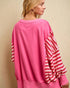 Woman wearing a pink outfit with red and white striped sleeves against a beige background