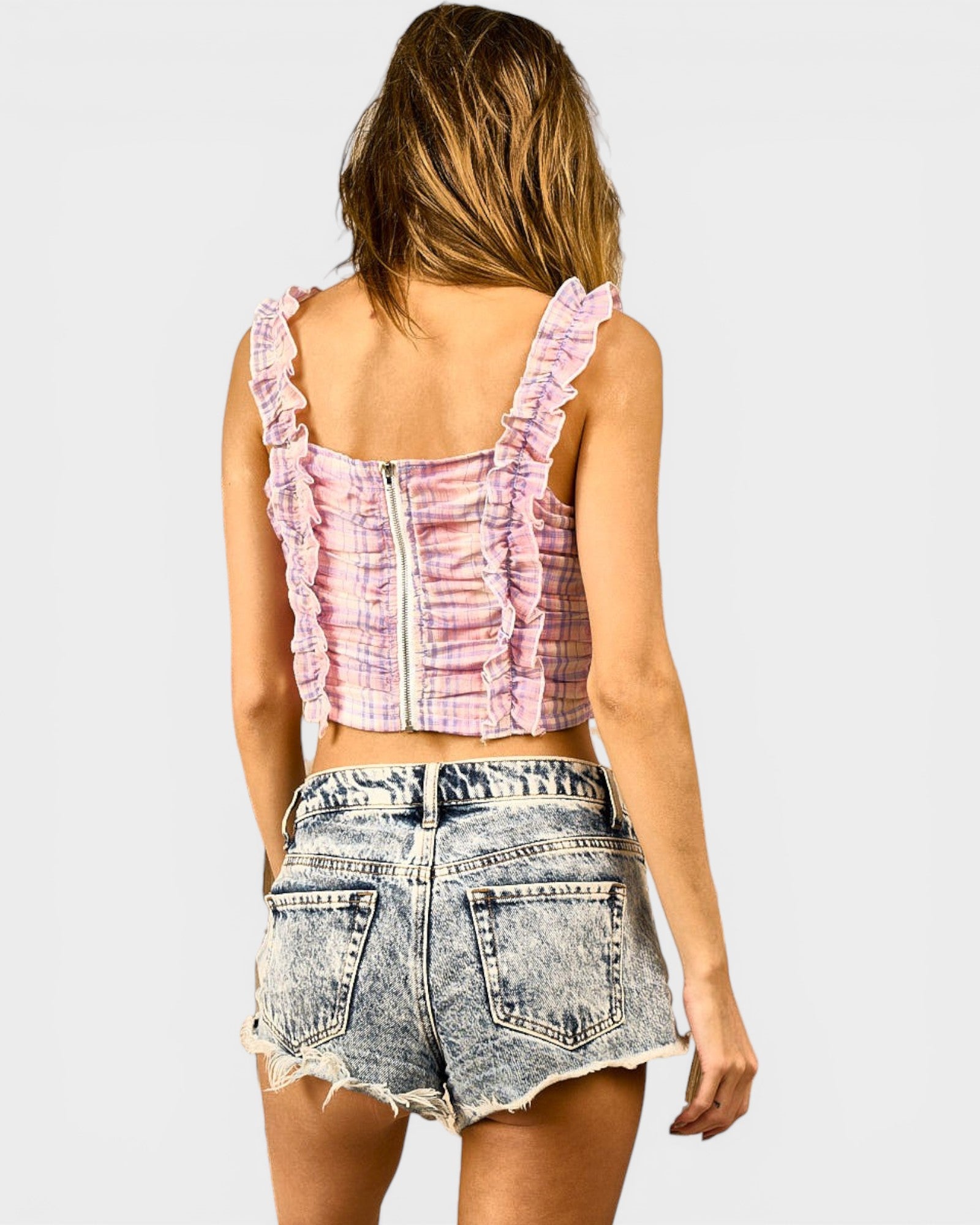 Woman wearing a pink tie-dye crop top and denim shorts on a white background