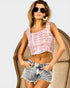 Woman wearing a pink plaid crop top and denim shorts, sitting on a chair.