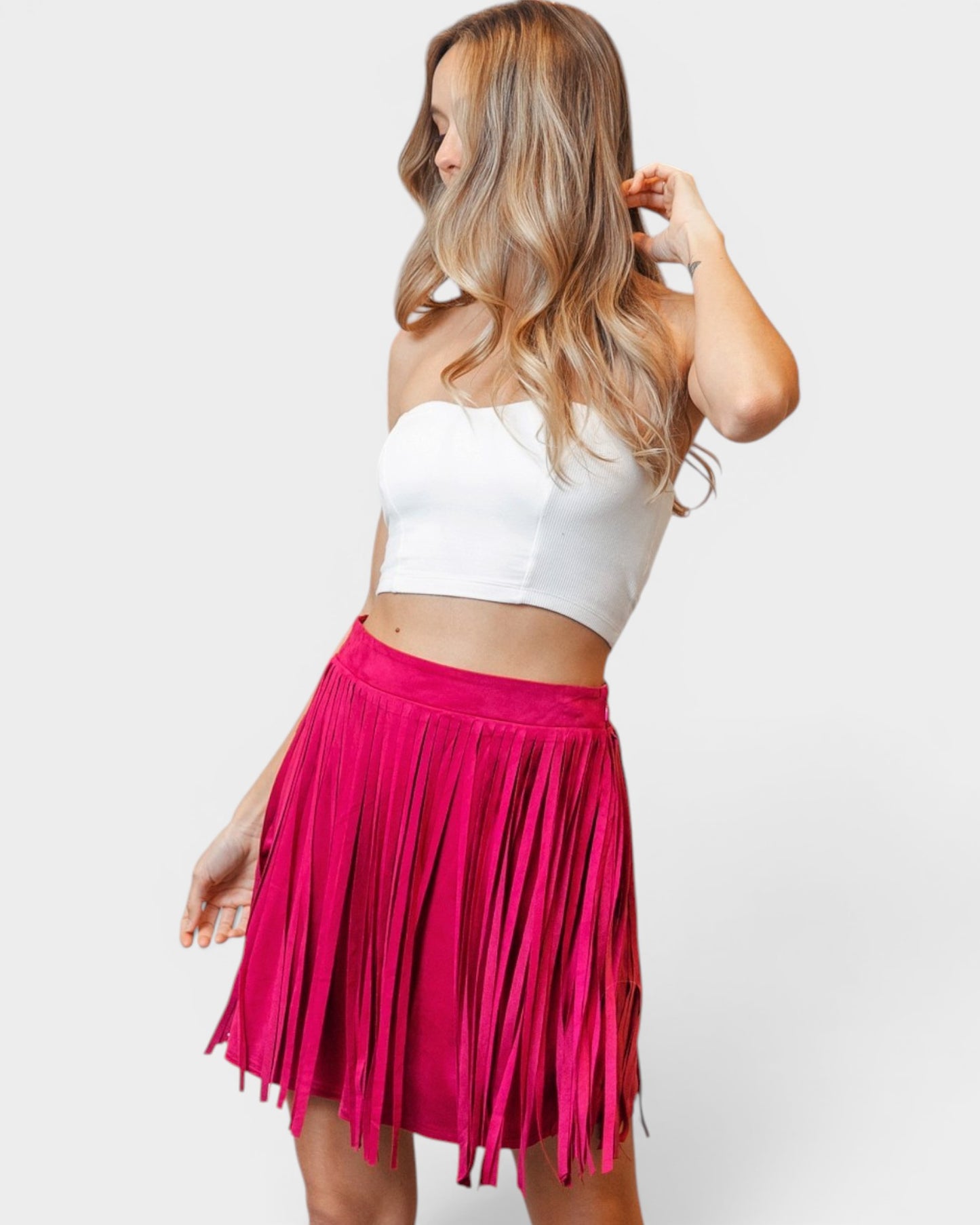 Woman wearing a white crop top and pink fringed skirt on a white background