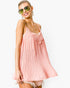 A woman wearing a light pink pleated camisole dress with lace trim at the neckline, styled with green-tinted sunglasses and dangling earrings against a plain white background.