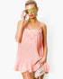 A woman wearing a light pink pleated camisole top with floral lace trim at the neckline, styled with distressed denim shorts and green-tinted sunglasses against a plain white background.
