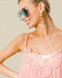 Woman wearing a pink lace dress with sunglasses and earrings against a neutral background