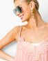 A close-up of a woman wearing a light pink pleated camisole top with floral lace trim, gold-framed sunglasses, and dangling earrings against a plain white background.