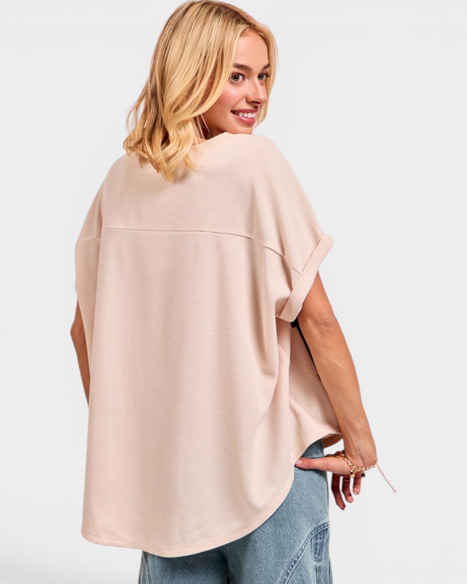Woman wearing a beige oversized top and blue jeans on a white background