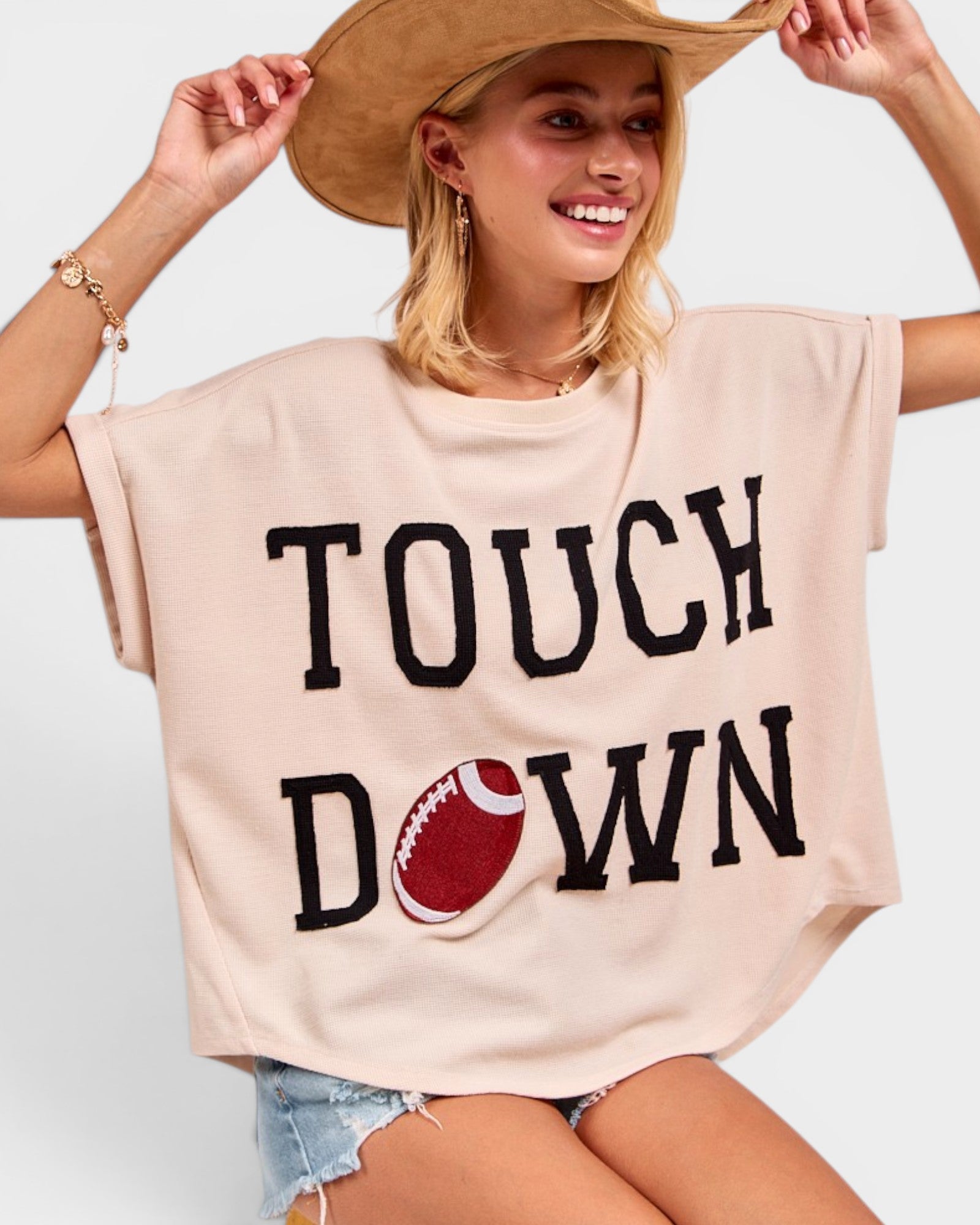 Woman wearing a beige oversized t-shirt with 'Touchdown' and a football graphic, smiling and posing.