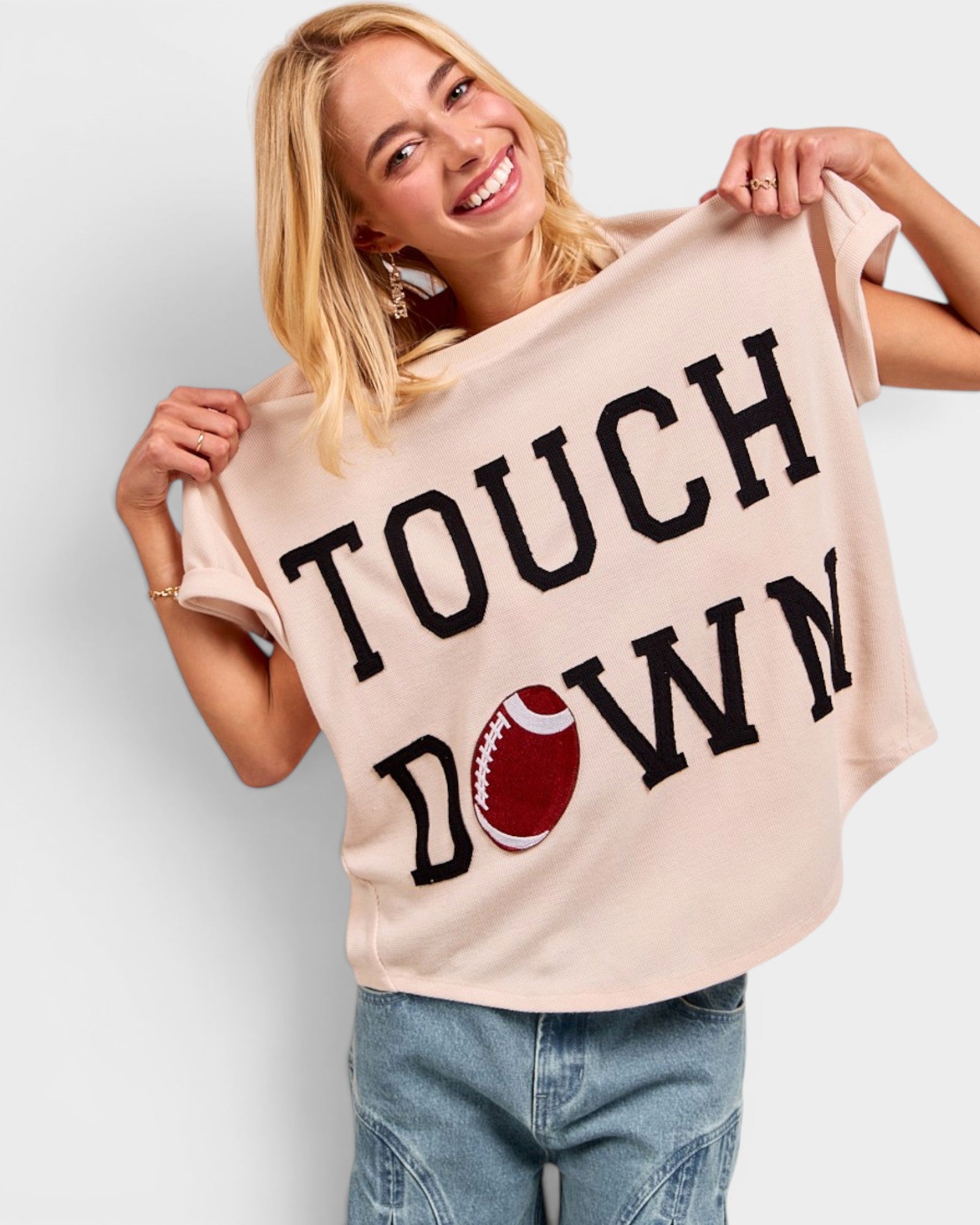 Woman holding a beige t-shirt with 'TOUCHDOWN' and a football graphic.
