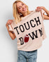 Woman holding a beige t-shirt with 'TOUCHDOWN' and a football graphic.