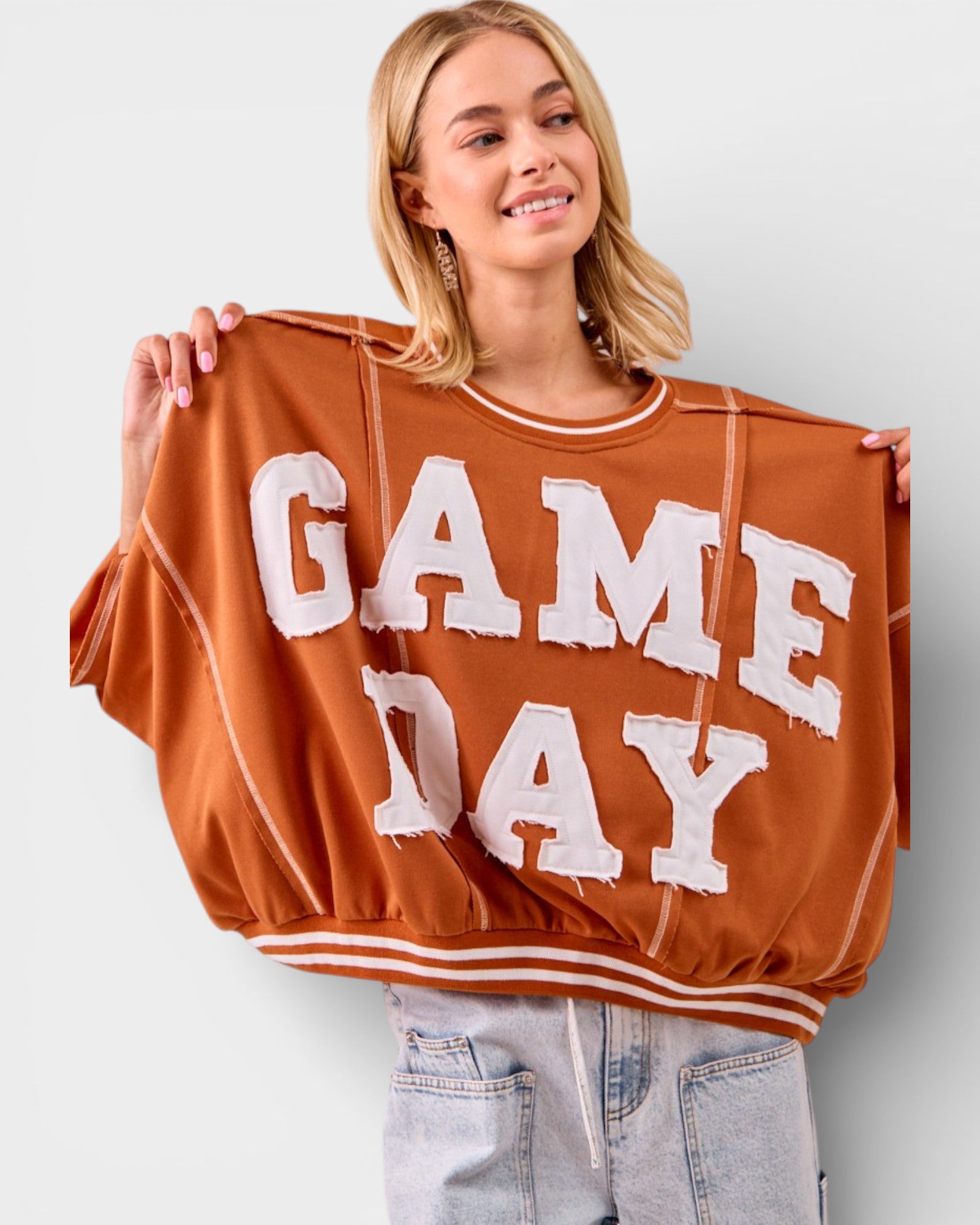 Woman wearing a brown 'GAME DAY' sweatshirt against a plain background