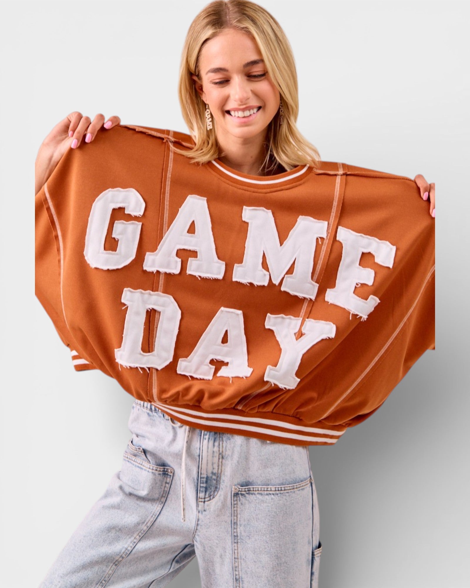 Person holding up a brown 'GAME DAY' sweatshirt against a plain background