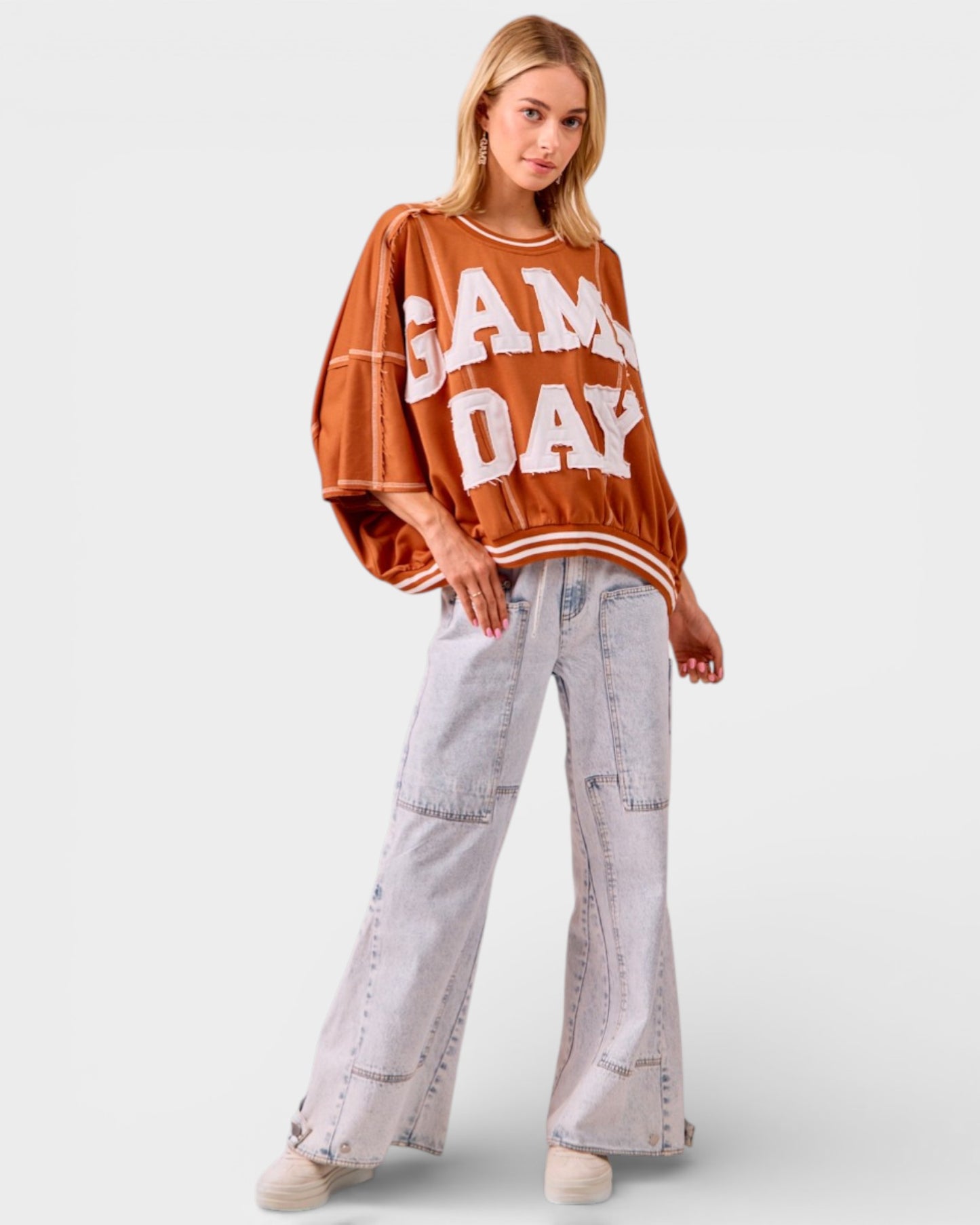 Woman wearing a 'Game Day' sweater and light gray pants on a white background