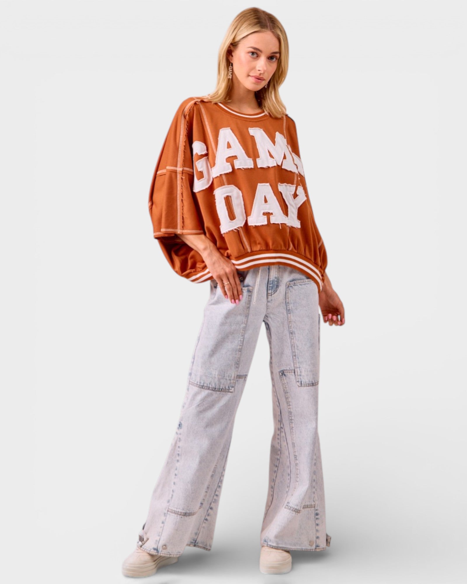 Woman wearing a 'Game Day' sweater and light gray pants on a white background