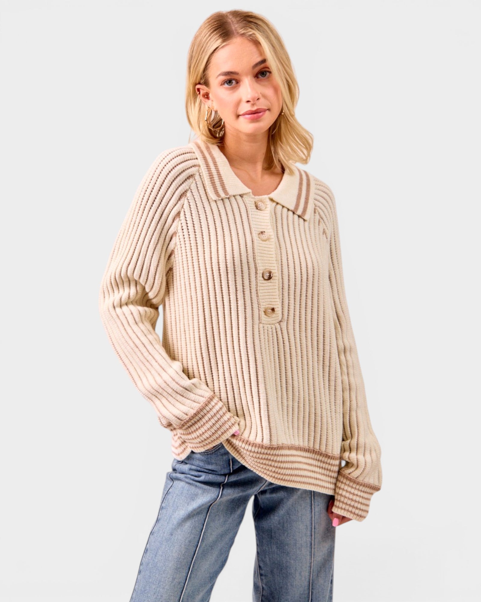 Woman wearing a beige ribbed sweater and blue jeans on a white background