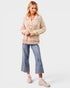 Woman wearing a beige ribbed sweater, blue jeans, and pink sneakers on a white background