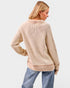 Woman wearing a beige ribbed sweater and blue jeans on a light gray background