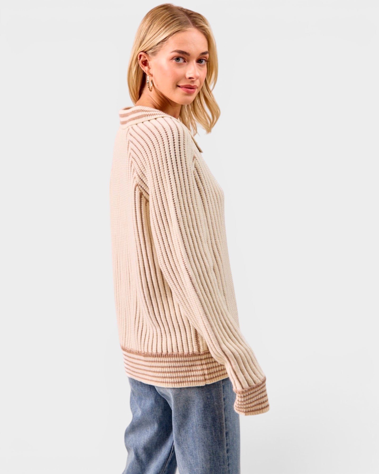 Woman wearing a beige ribbed sweater and blue jeans on a white background