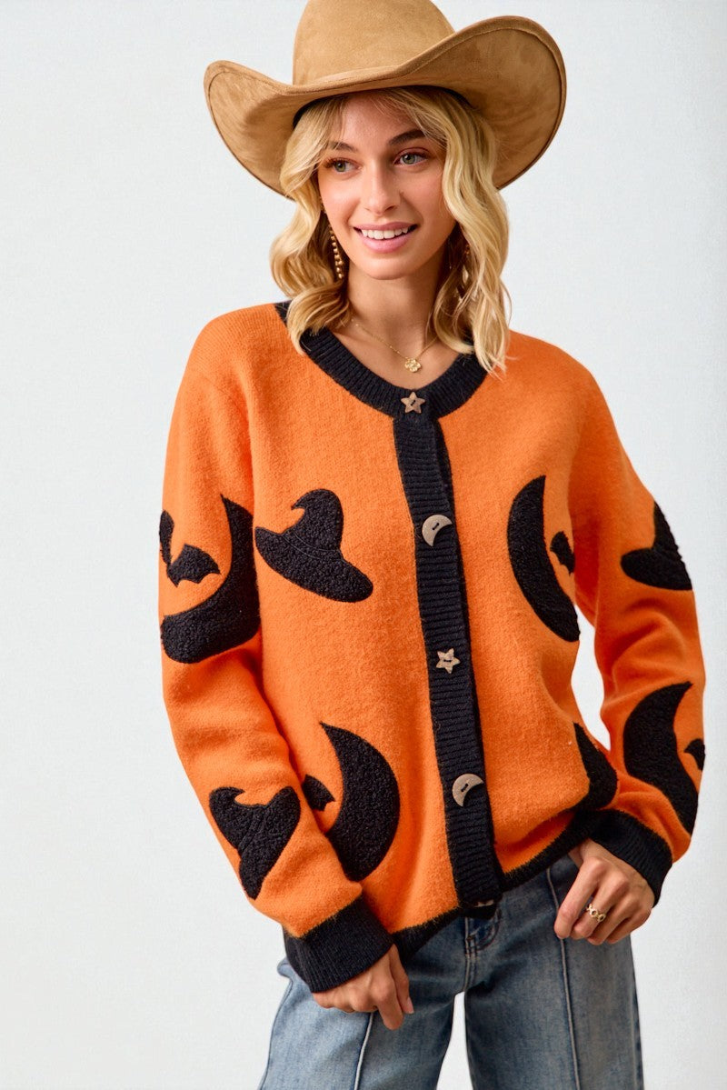 Person wearing an orange sweater with black cat designs and a cowboy hat on a white background