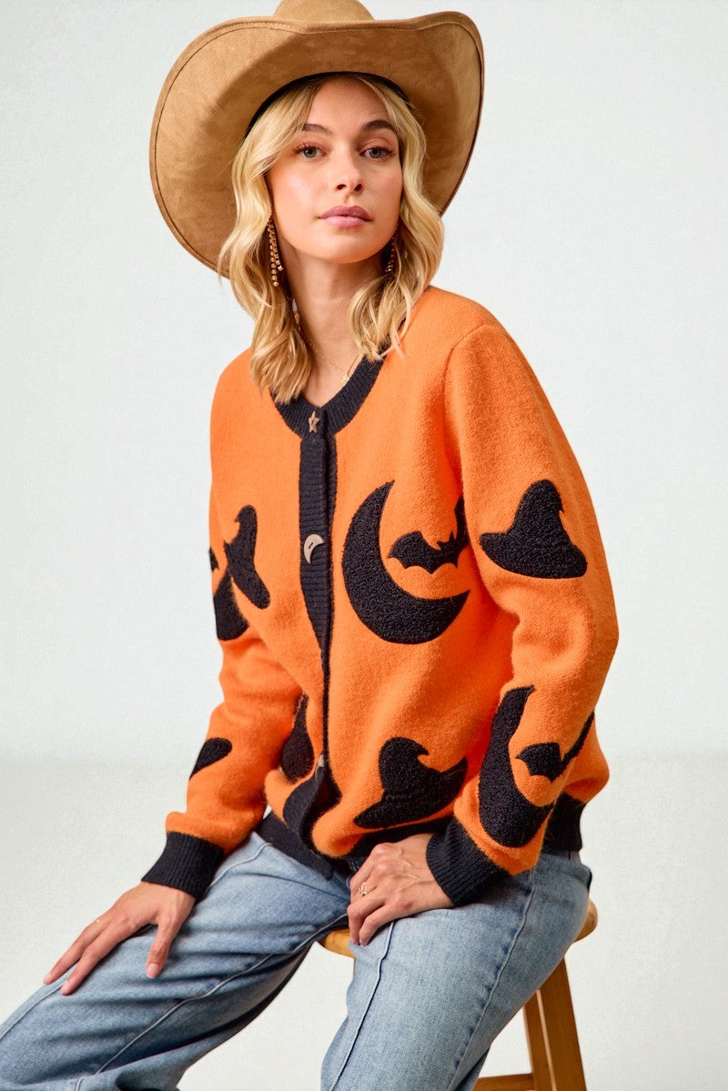 Woman wearing an orange sweater with black moon designs and a brown hat on a white background