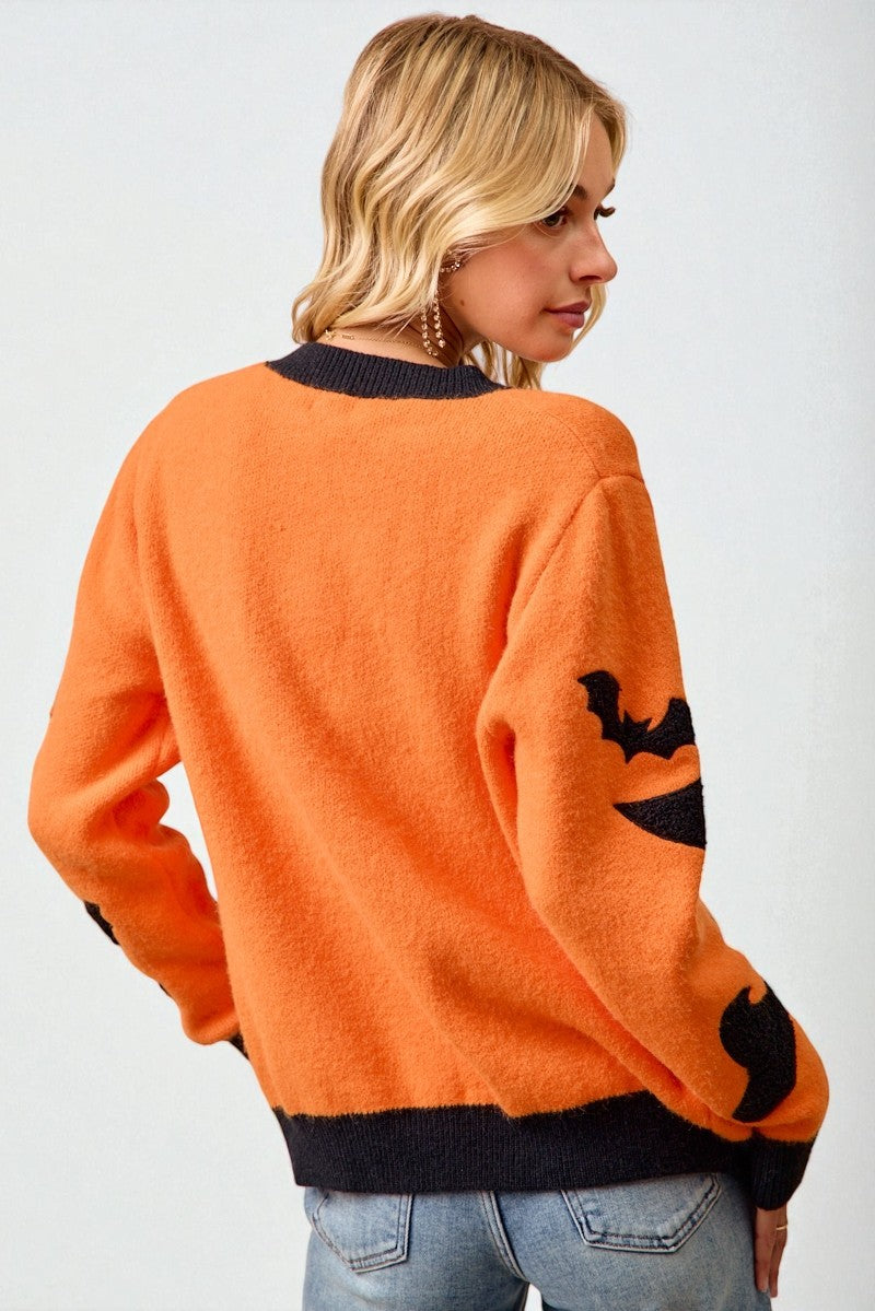 Person wearing an orange sweater with black cat designs on a plain background